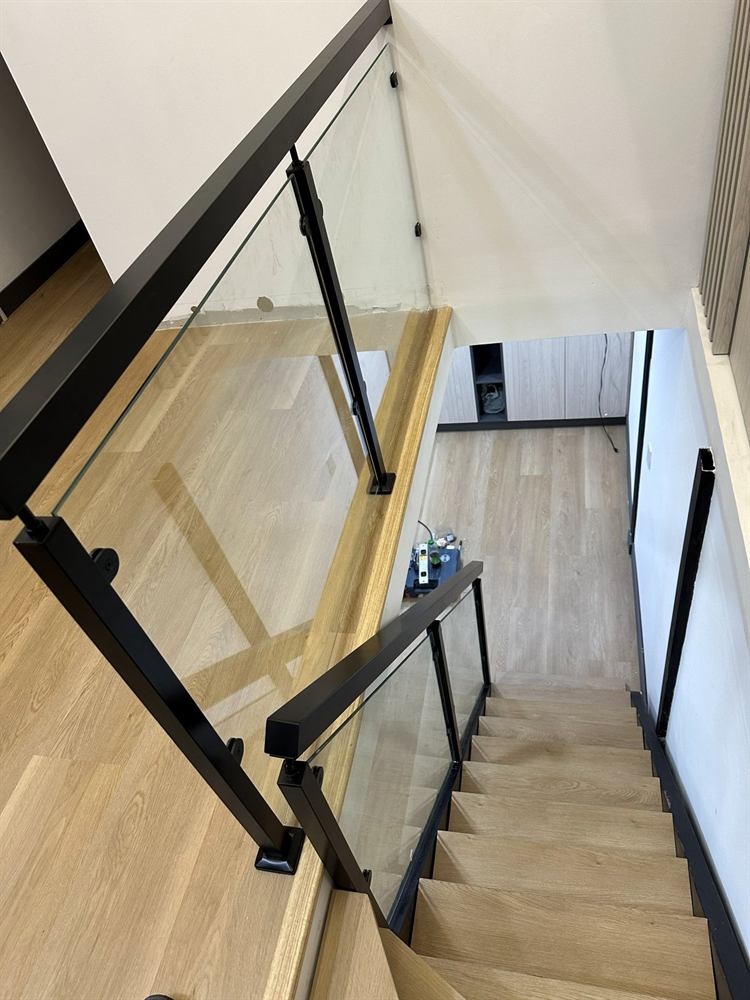 Baranda de vidrio con pasamanos negro en una escalera de madera