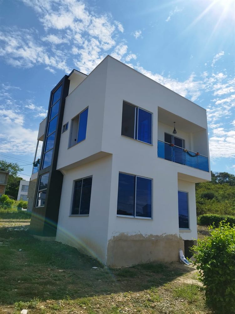 Casa de dos pisos con ventanales azules y baranda de vidrio en el balcón