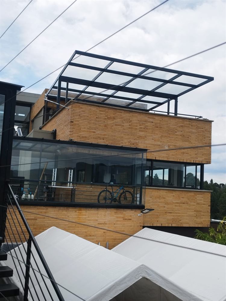 Marquesina de vidrio con estructura negra sobre la terraza de una casa de ladrillo