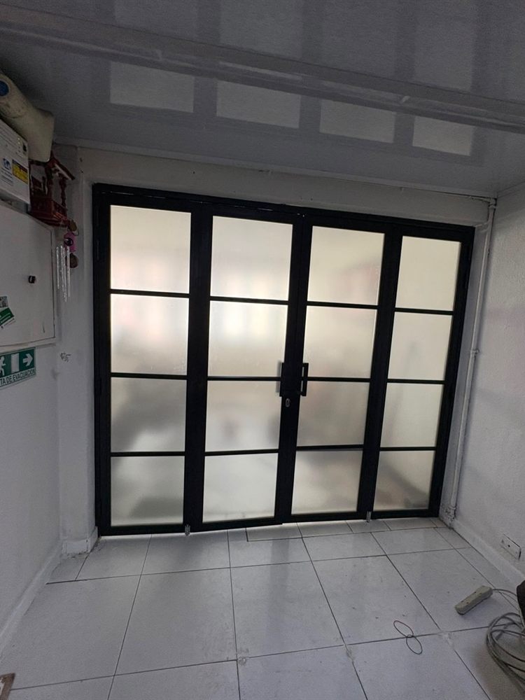 Puerta en acordeón de aluminio negro con vidrio esmerilado